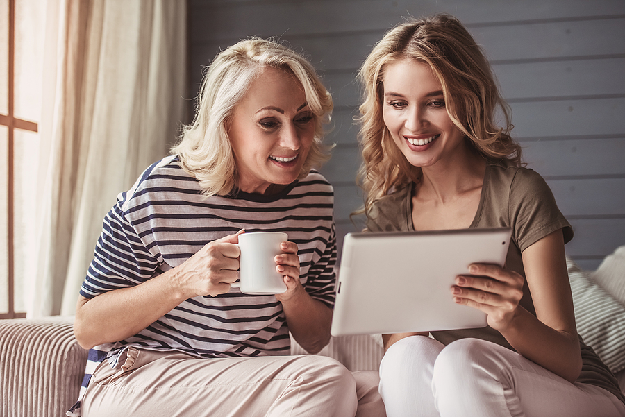 An adult daughter shows her mother something on a tablet.