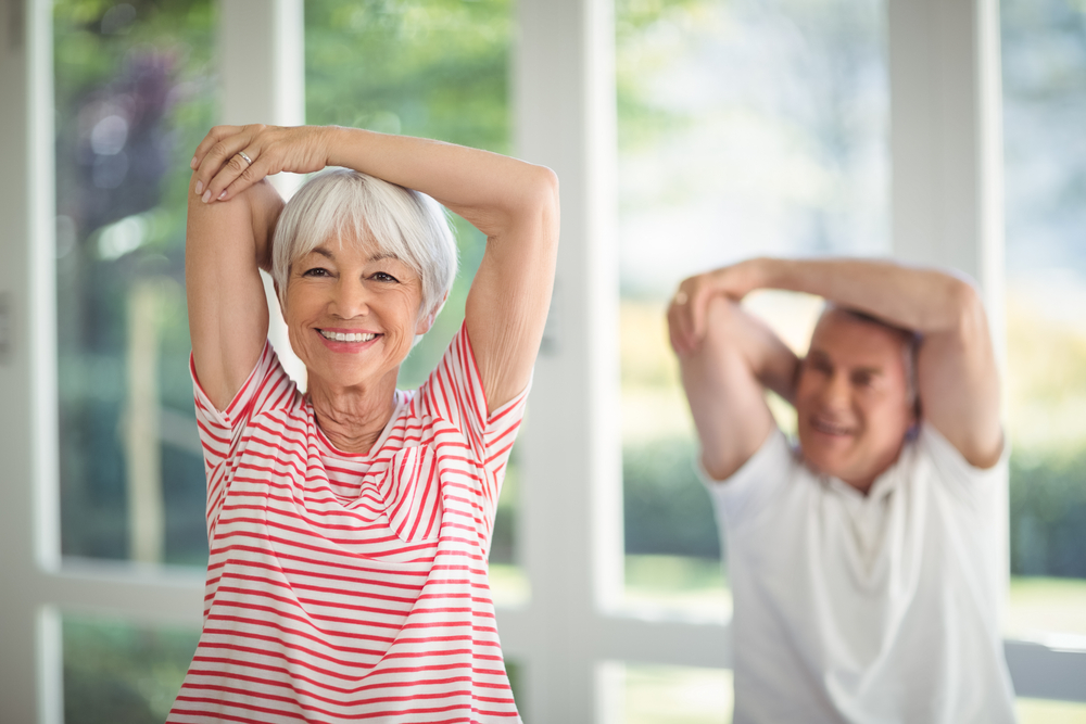 A senior woman and senior man stretching their arms