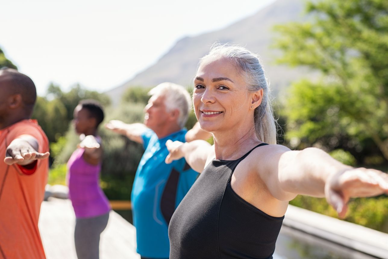 A senior woman enjoying a yoga class outside and learning balance exercises.