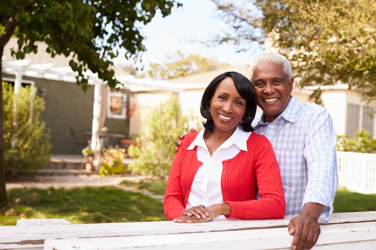 Senior black couple look to camera outside their new house