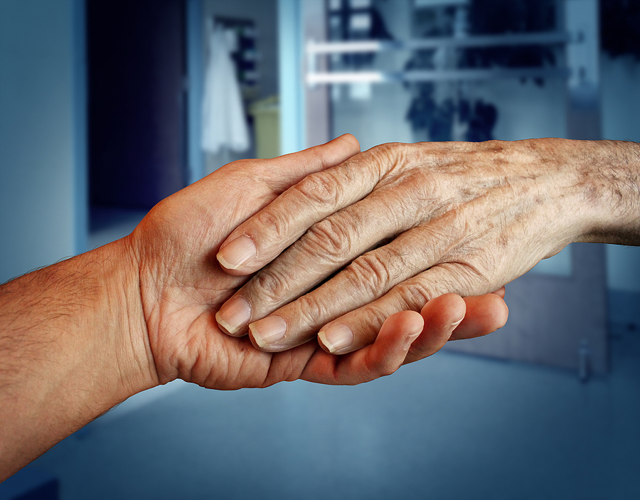 An adult child holds an older adult’s hand as they discuss memory care services