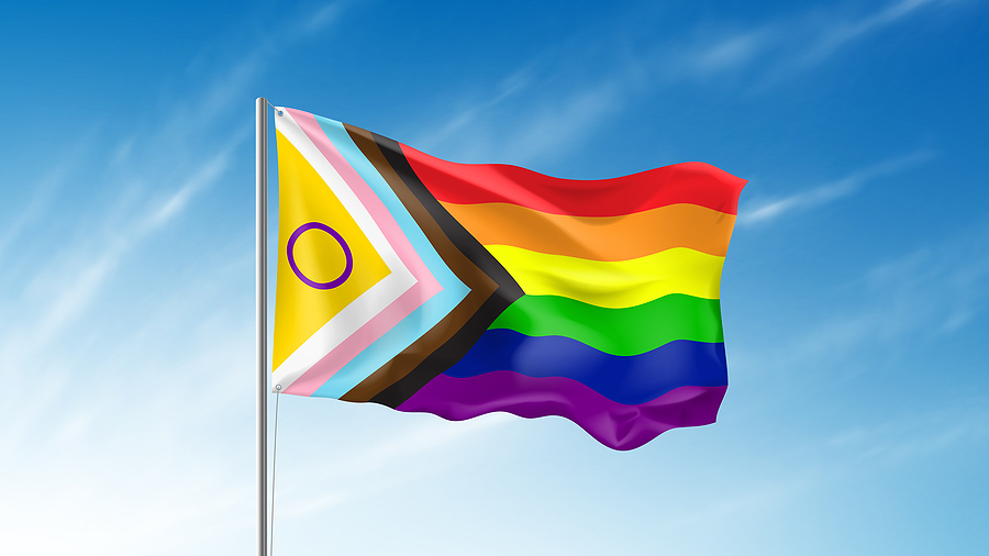 Inclusive pride flag waving in wind against blue sky