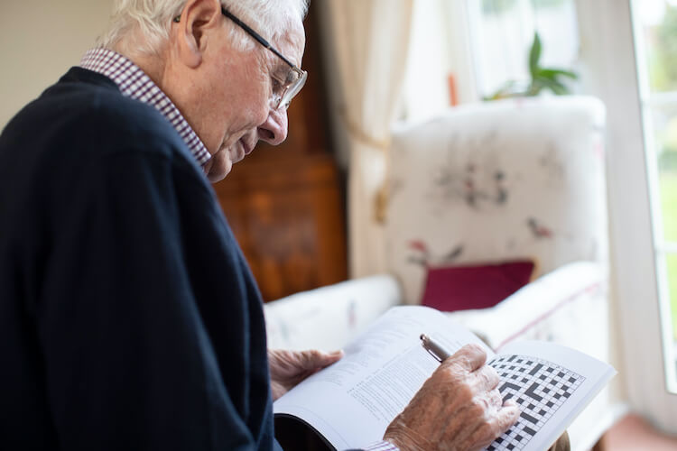 Senior man completing a crossword puzzle to improve his brain health.