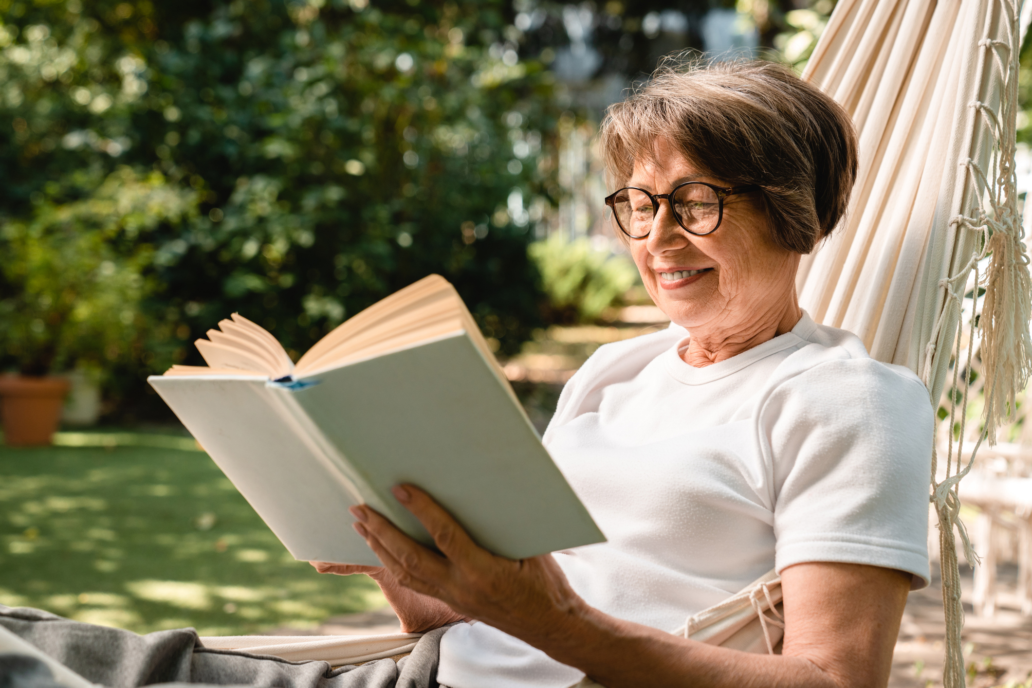 A senior woman reads a book outside in a hammock
